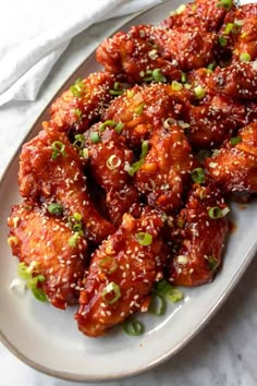 a white plate topped with chicken wings covered in sesame seeds and green onion sprinkles