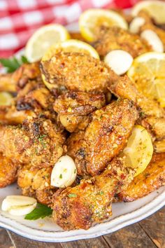 fried chicken with lemons and garlic on a white plate next to a red checkered tablecloth