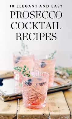 two glasses filled with pink cocktail sitting on top of a wooden table next to a tray