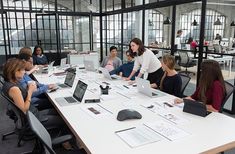 a group of people sitting around a table with laptops on it and papers in front of them