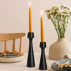 two candles are sitting next to each other on a table with plates and flowers in the background