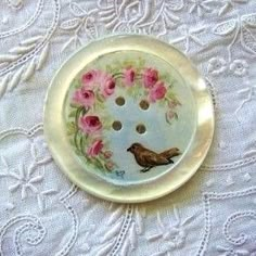 a button with pink flowers and a bird on it sitting on a lace tablecloth