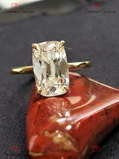 a yellow diamond ring sitting on top of a piece of red coral with gold accents