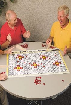 three men sitting at a table playing a board game with red and yellow letters on it