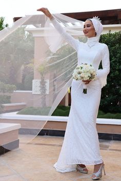 a woman in a white dress and veil posing for the camera with her hands up