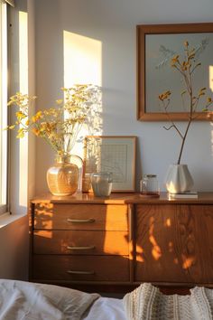 two vases with flowers sit on a dresser next to a window in a bedroom