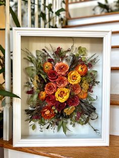 an arrangement of flowers is framed in a white frame on the stairs at this home