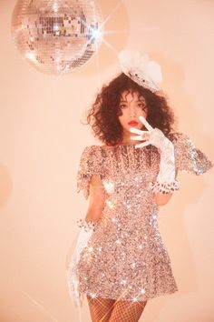 a woman with curly hair wearing a silver dress and holding a disco ball in her hand