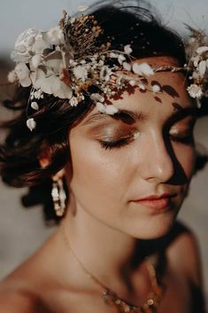 a woman with flowers in her hair is wearing a necklace and headpiece on the beach