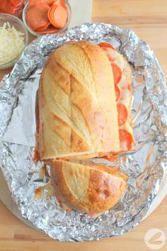 the sandwich is cut in half and sitting on tin foil with carrots next to it