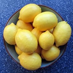 a bowl filled with yellow lemons on top of a blue counter