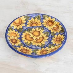 a blue and yellow bowl with sunflowers painted on the side, sitting on a white surface