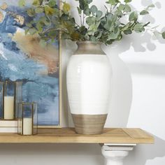 a white vase sitting on top of a wooden shelf next to a painting and candles