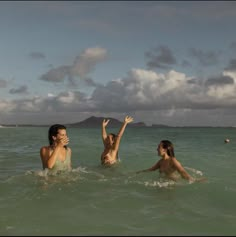 three girls in the ocean playing with a frisbee and one girl holding her hand up