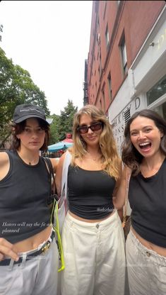 three young women standing next to each other in front of a building with their mouths open