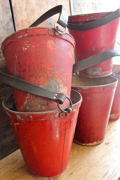 three red buckets sitting on top of a wooden table next to each other with straps around them