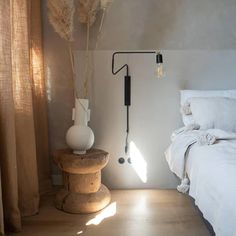 a room with a bed, lamp and vase on the floor in front of it