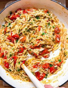 pasta with tomatoes and parmesan cheese in a skillet being stirred by a spatula