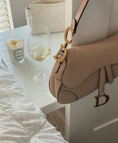 a handbag sitting on top of a white table next to a glass of wine