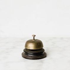 an old brass bell on a marble countertop with white walls in the backround