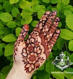 a hand with henna on it and some green leaves in the backgroud