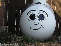 a white toilet sitting in the grass next to a wooden fence with a face painted on it