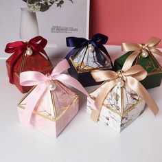 four different colored boxes with bows and pearls on them sitting next to a vase filled with flowers