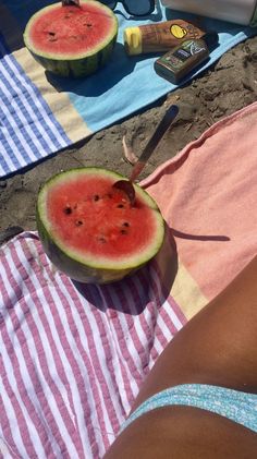 a watermelon cut in half sitting on a beach towel next to other items