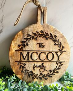 a wooden sign that says the mccy family hanging on a wall next to some plants