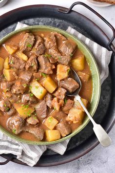 a bowl filled with stew and potatoes on top of a white table next to bread