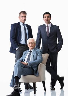 two men in suits and ties are posing for a photo with an older man sitting on a chair