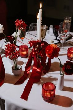 the table is set with candles and red flowers in vases, which are adorned with satin ribbons