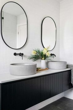 two round mirrors are above the sinks in this bathroom with black and white tiles on the walls