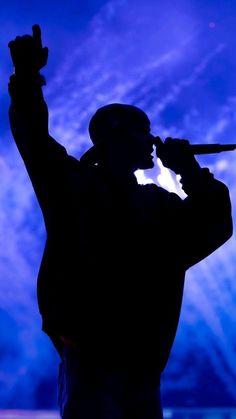 the silhouette of a man holding a microphone in front of a blue sky with clouds