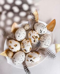 a white plate topped with eggs covered in black and gold speckles next to feathers