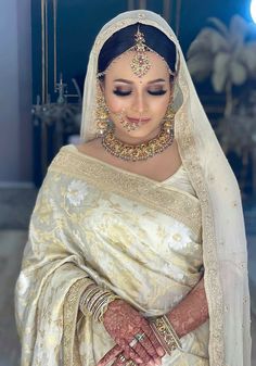 a woman wearing a white and gold bridal outfit with her hands on her chest