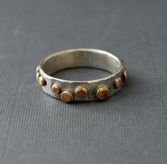 This comfortable ring is simple with a fun flair. It can be casual or elegant, depending on where you are. The band is hammered sterling silver. Flattened bronze balls have been soldered to the band.  Since each ring is hand made individually, the dots will vary in size and placement. This ring will be made to your size within two weeks of ordering. I offer a full money back guarantee (or exchange) if for any reason your ring does not fit. SIZE:  The band is 5.5mm wide and just over 1mm thick (18 gauge). The dots add about another mm to the thickness. If you do not see your ring size in Options, please choose the closest size and include a note. I will work with you to create a ring in your size. I happily accept layaway. Please look at my payment policies or send me a message for more inf Silver Ring Band, Hammered Silver Ring, Kay Jewelry, Hammered Ring, Hammered Rings, Hammered Sterling Silver, Stacked Bangles, Copper Bracelet, Silver Band Ring