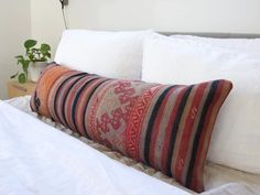 a bed with white linens and pillows on top of it next to a plant