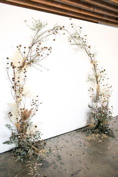 an arch made out of branches and flowers on the floor in front of a white wall