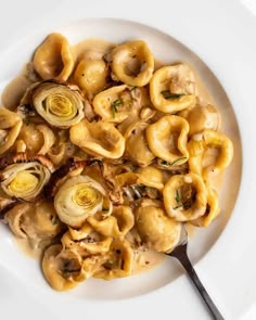 a white plate filled with pasta and artichokes on top of a table