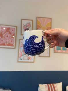 a person is holding a coffee cup in front of pictures on the wall behind them