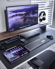 a computer desk with a phone, keyboard and headphones on it next to a monitor