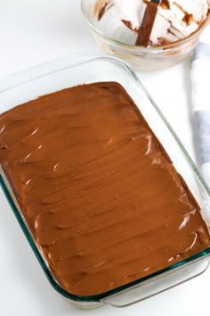 a chocolate cake in a glass baking dish next to a knife and bowl of whipped cream