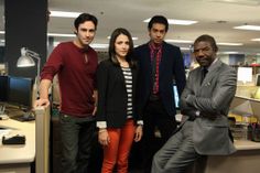 four people standing in an office with one person wearing a suit and the other looking at the camera