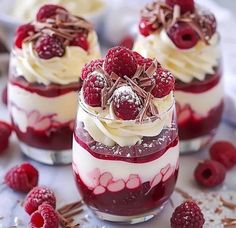 three desserts with raspberries and whipped cream in them on a white table