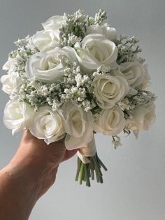 a hand holding a bouquet of white roses