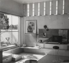 a black and white photo of a living room with furniture in the foreground, windows on the far wall