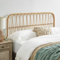 a bed with white linens and a rattan headboard on the nightstand next to it