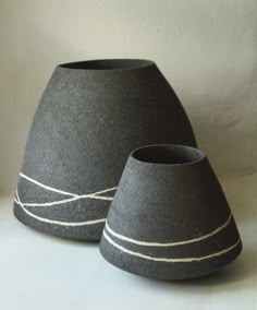 two black vases sitting side by side on a white tableclothed surface with lines drawn across them