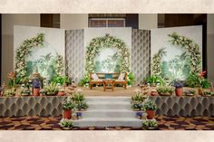 a stage set up for a wedding ceremony with flowers and greenery on the wall